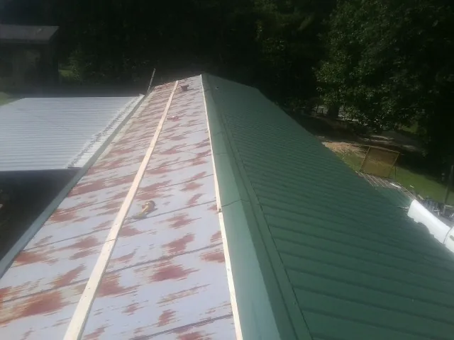 Old rusted panels beside newly installed green metal roofing — Wind Damage Roof Repair by Roofing Brothers in Coral