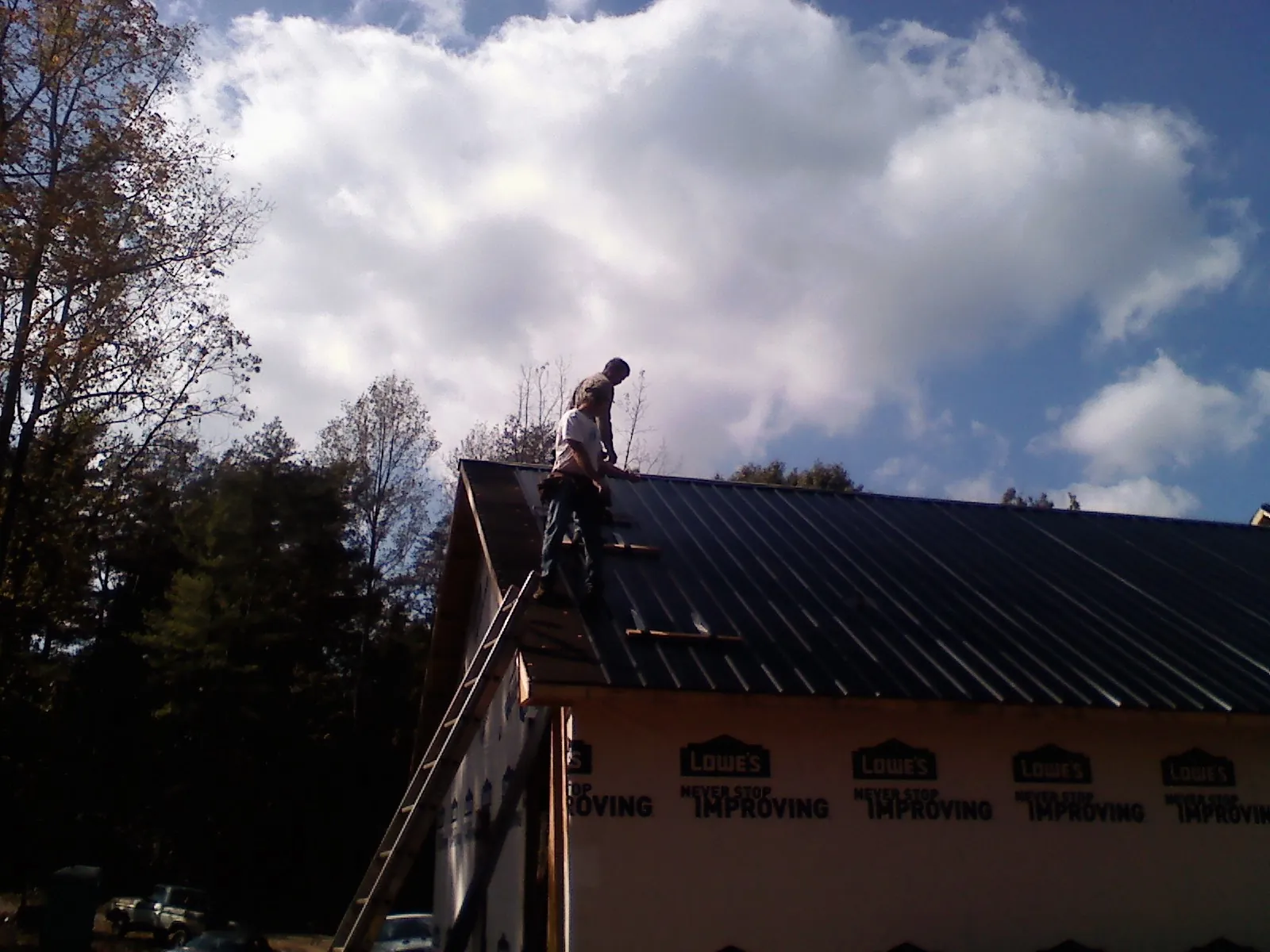 Roofer fastening dark metal panels high against a cloudy sky, from a Roof Inspection job in Coral