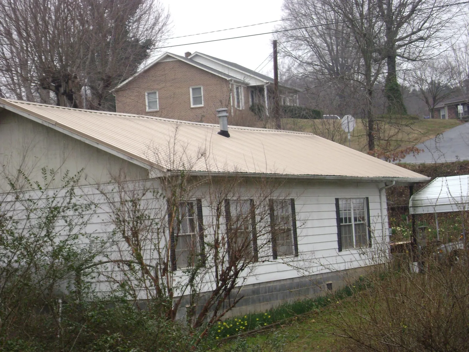 Tan metal roof on a white sided house set into a hillside — Commercial Roofing by Roofing Brothers in Coral